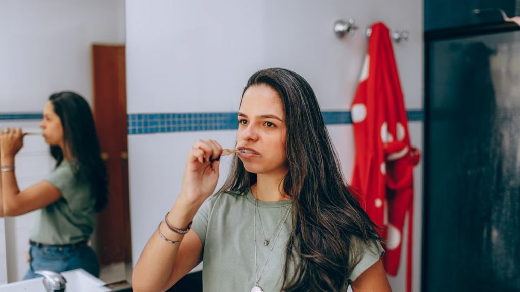 Young woman brushing teeth in a modern bathroom with a red towel hanging nearby.